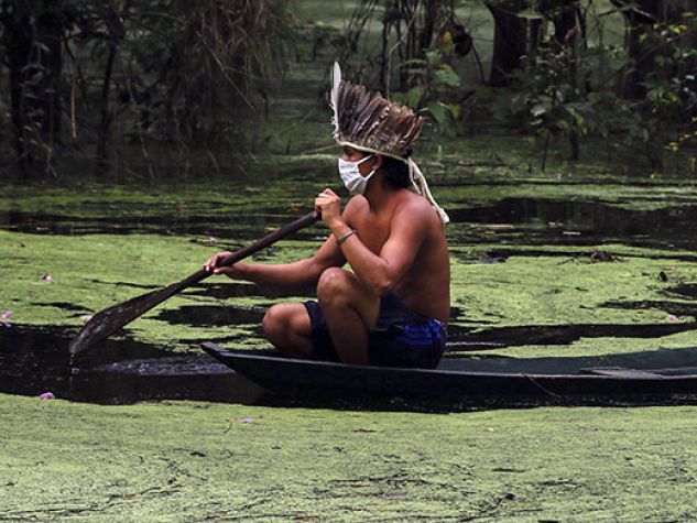 Due indios con mascherine chirurgiche su canoa in un corso d'acqua nella foresta amazzonica.