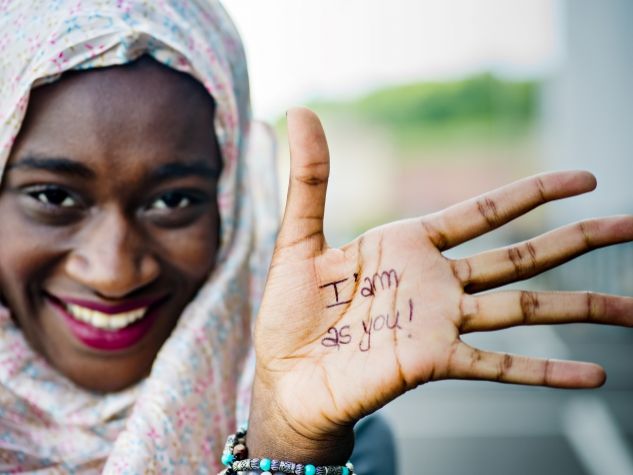 donna migrante mostra il palmo della mano con la scritta "io sono come te"