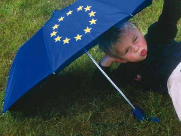 bambino steso su un prato protetto da ombrello con simbolo Unione Europea