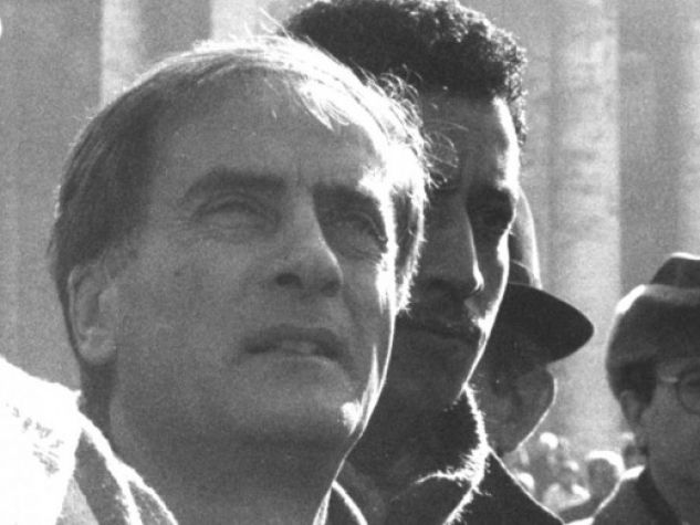 Don Luigi Di Liegro fianco a fianco con alcuni immigrati. Sullo sfondo s’intravvede il colonnato di piazza San Pietro, in Vaticano. 
