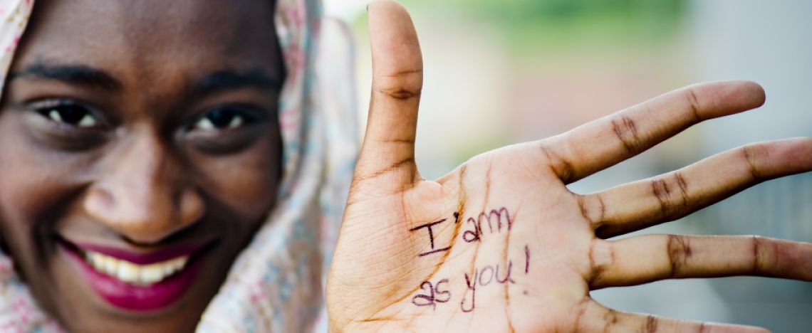 donna migrante mostra il palmo della mano con la scritta "io sono come te"