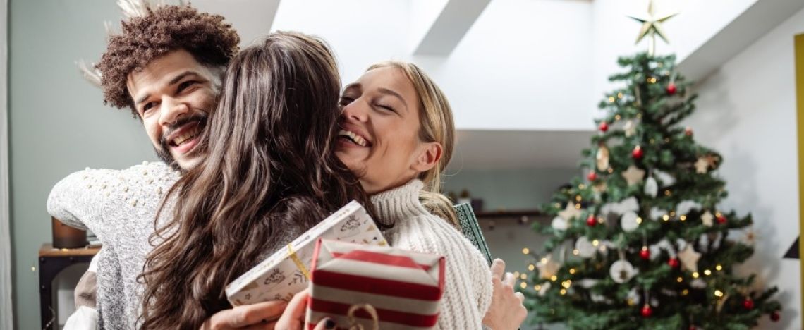 Un ragazzo e due ragazze si scambiano abbracci e regali a Natale.