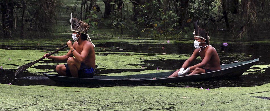 Due indios con mascherine chirurgiche su canoa in un corso d'acqua nella foresta amazzonica.